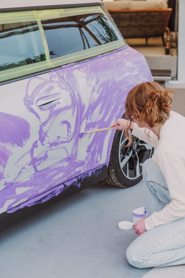 Madelen Möllard kneeling beside the MINI Cooper, laying a purple ground colour across the car door with a brush